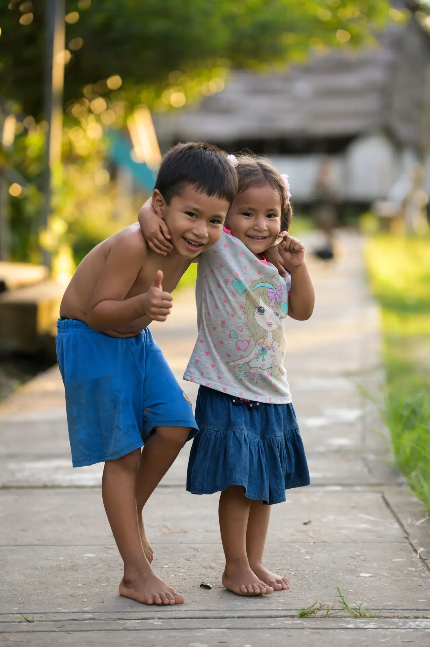 Deux jeunes enfants posent en riant sur un chemin de village.